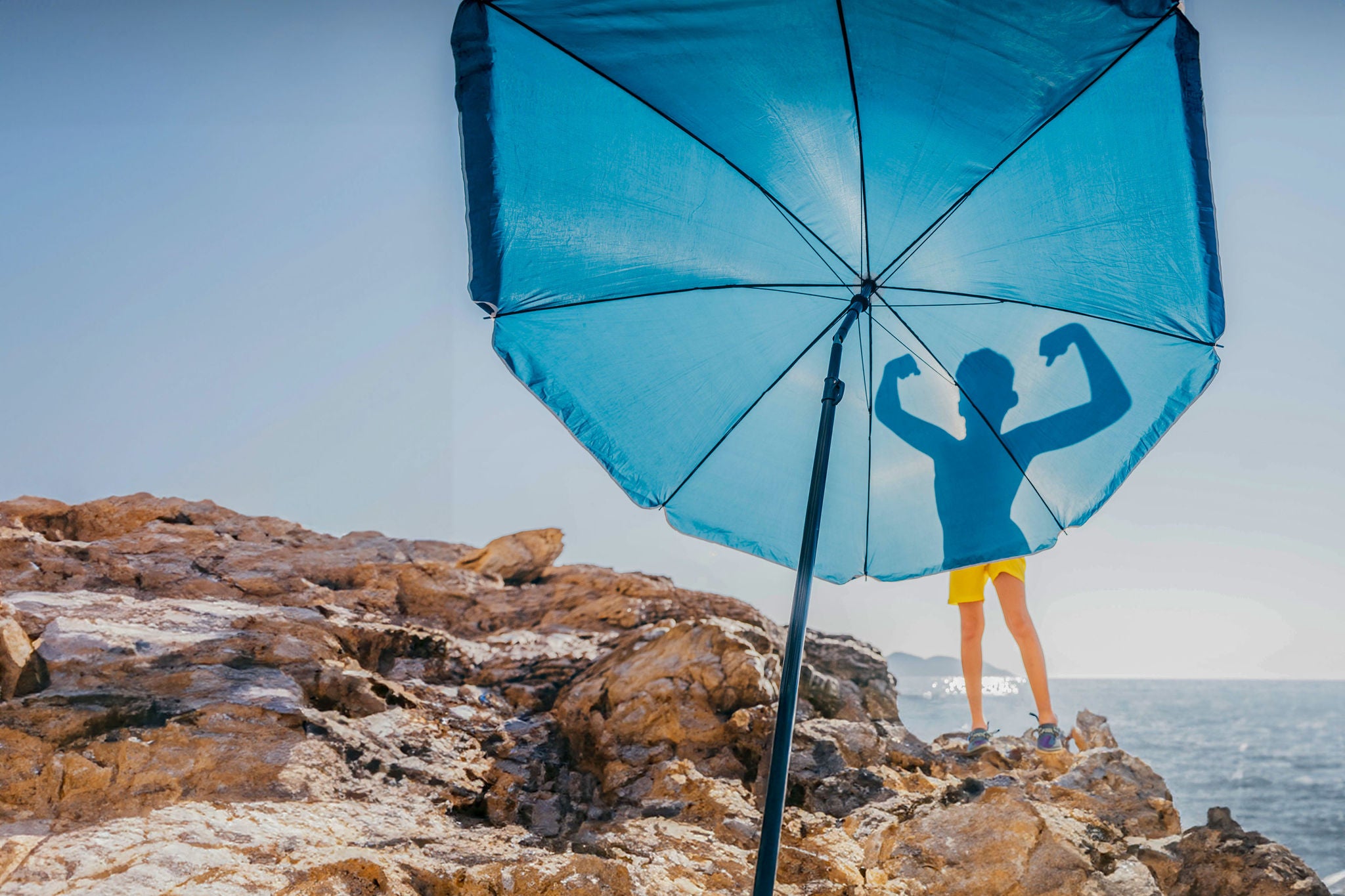 Silhouette of boy flexing his muscles on blue beach umbrella